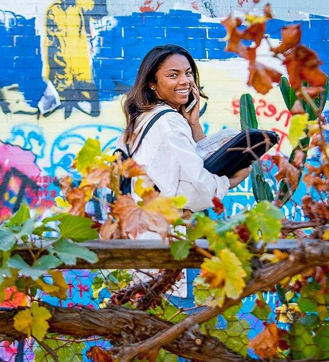 a student walks in front of the free wall and smiles at the camera